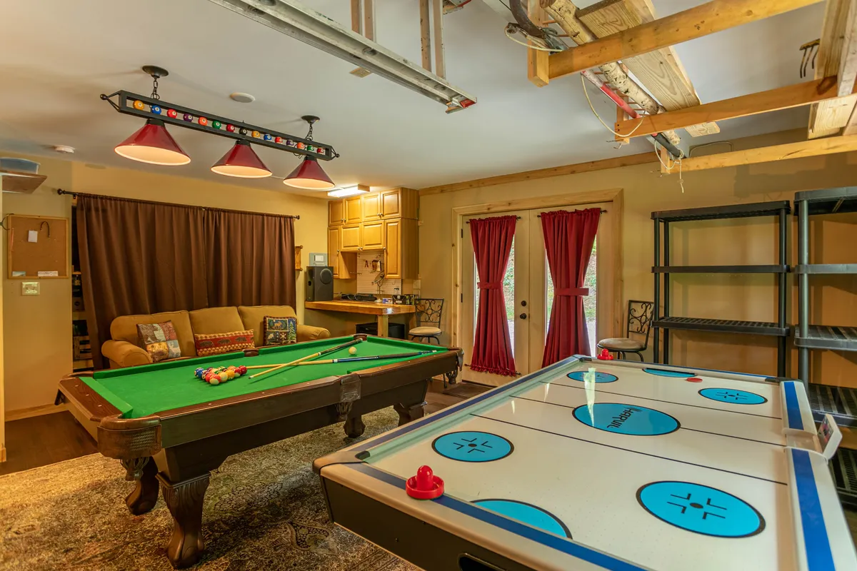 The image shows a fun and relaxed game room with a pool table and air hockey table, a cozy sofa for spectators or participants, and soft curtains lending a touch of comfort. The setting exudes an air of camaraderie and shared enjoyment.