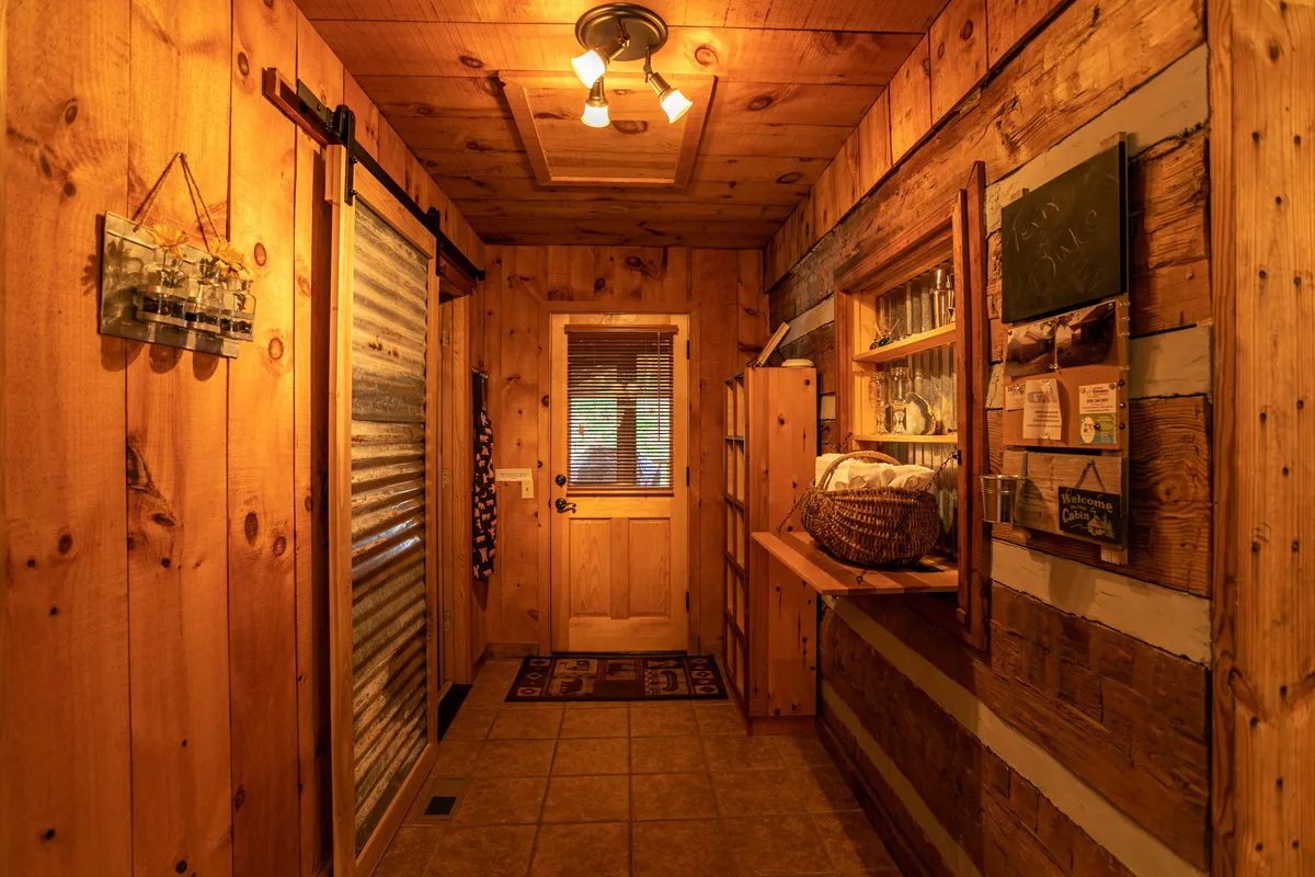 An inviting entryway with warm wooden walls, a welcoming door, shelves filled with decorative items, and personal touches that evoke hospitality. The soft lighting and cozy atmosphere suggest a space where guests are greeted and memories are made.
