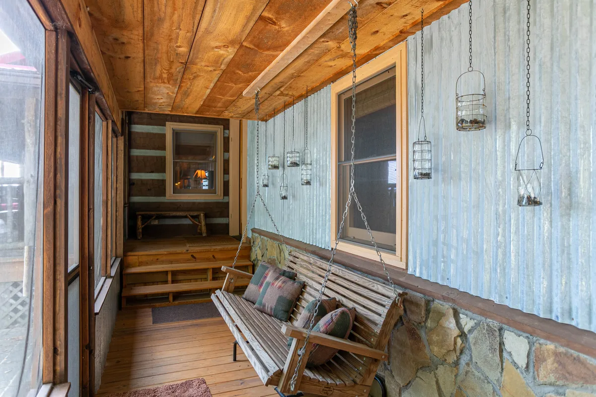 A cozy wooden swing suspended from the ceiling, adorned with soft pillows and illuminated by hanging lanterns. The swing is set against striped wooden walls, creating a tranquil indoor-outdoor space perfect for relaxation and conversations.