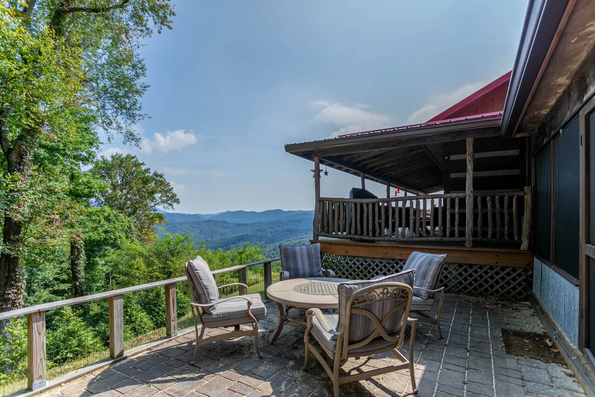 The image displays a spacious patio with comfortable outdoor furniture, a sturdy wooden railing, and panoramic mountain views stretching into the distance. The setup is ideal for alfresco dining, socializing, or simply enjoying the natural beauty throughout the seasons.