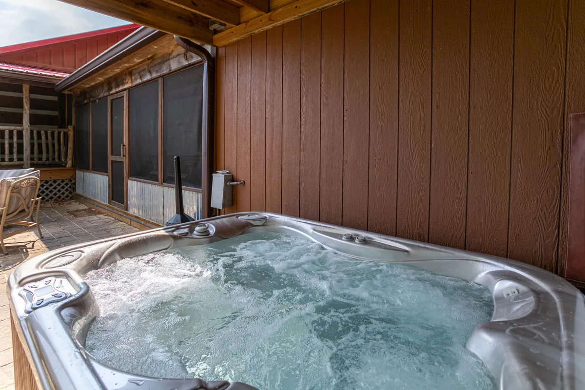 The image showcases a spacious wooden deck and screened porch, complete with a hot tub, all nestled within a tranquil natural setting. The deck connects directly to the outdoors, making it a versatile space for entertaining, relaxing after playtime, or gathering with pets and family.