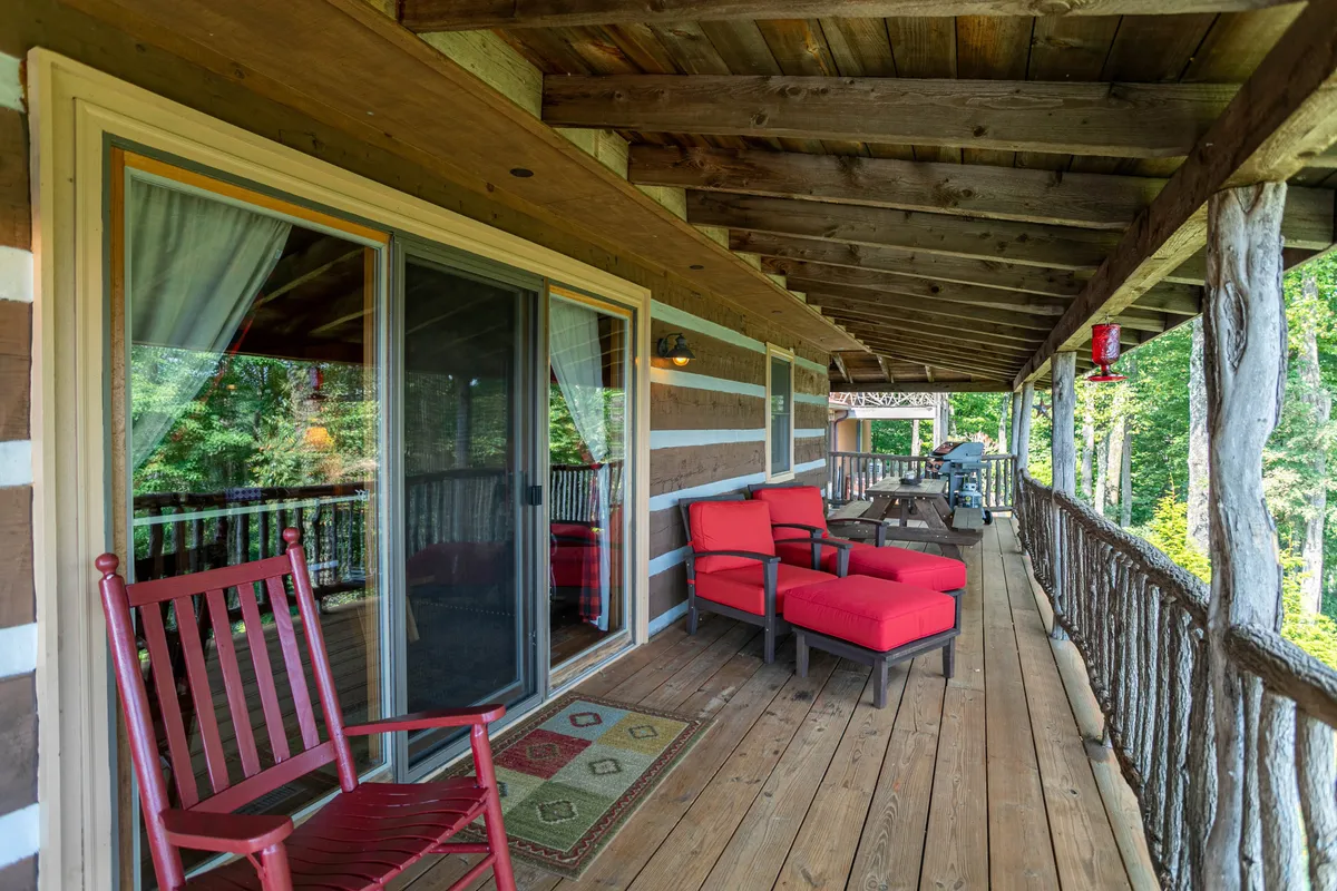 This image captures a porch area with red outdoor chairs, a wooden railing, and sliding glass doors, creating a cozy atmosphere for relaxing, reading, or enjoying a morning coffee surrounded by nature. The space feels intimate yet connected to the outdoors.