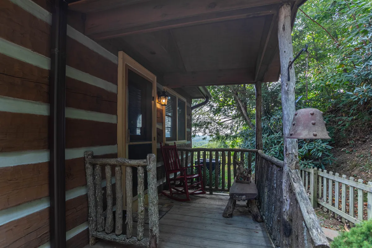 A cozy exterior shot featuring a wooden rocking chair on a rustic porch, complemented by a traditional railing, a hanging bell, and abundant natural greenery. The setting evokes moments of relaxation and connection with nature, perfect for unwinding after exploring local attractions.