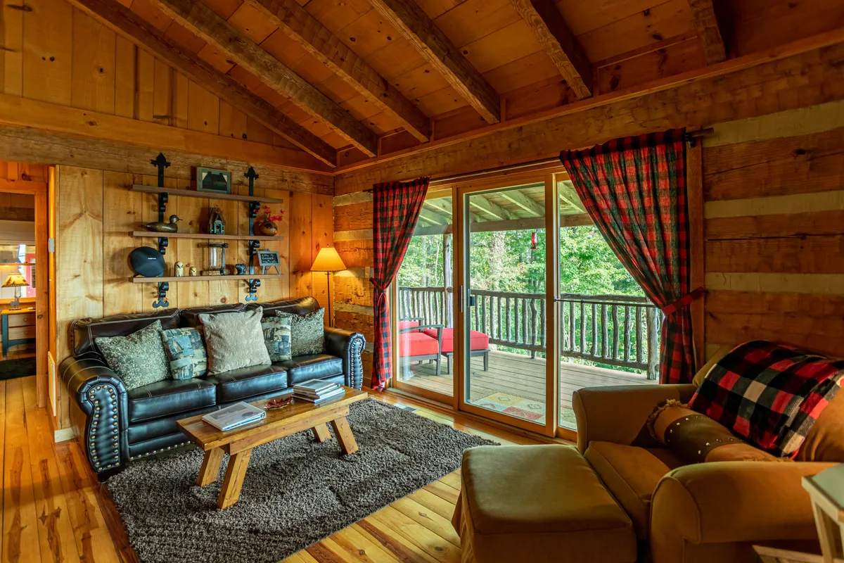 A cozy seating area with a leather sofa and wooden coffee table set before large windows, decorative shelving, and warm lighting. The natural light streaming in and the inviting furniture make it a perfect spot for relaxation and conversation.