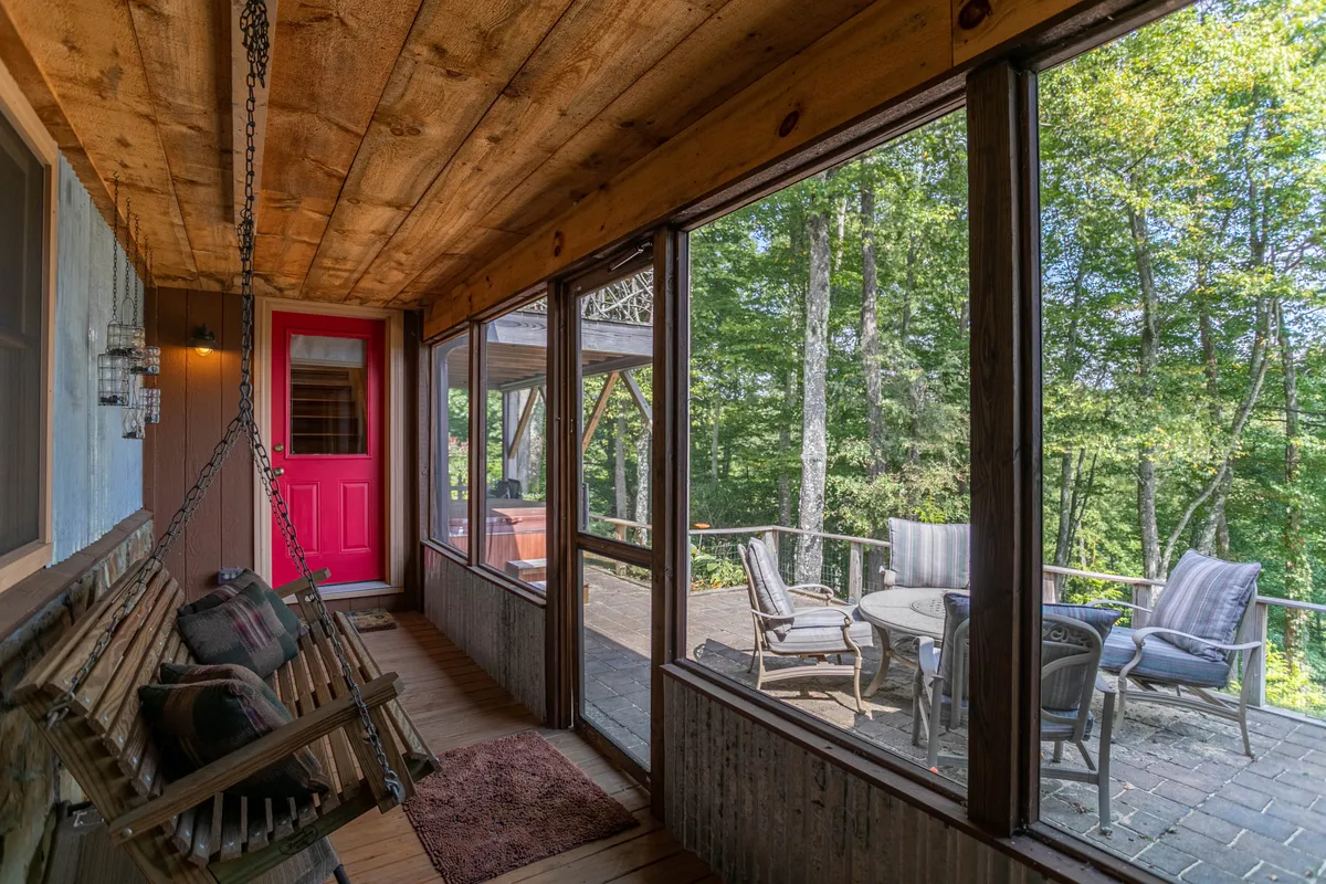 A charming porch scene featuring a swinging bench and a bright pink door, surrounded by an inviting outdoor seating area. The porch has direct access to nature and provides a welcoming, playful vibe that suits families and pet owners alike.