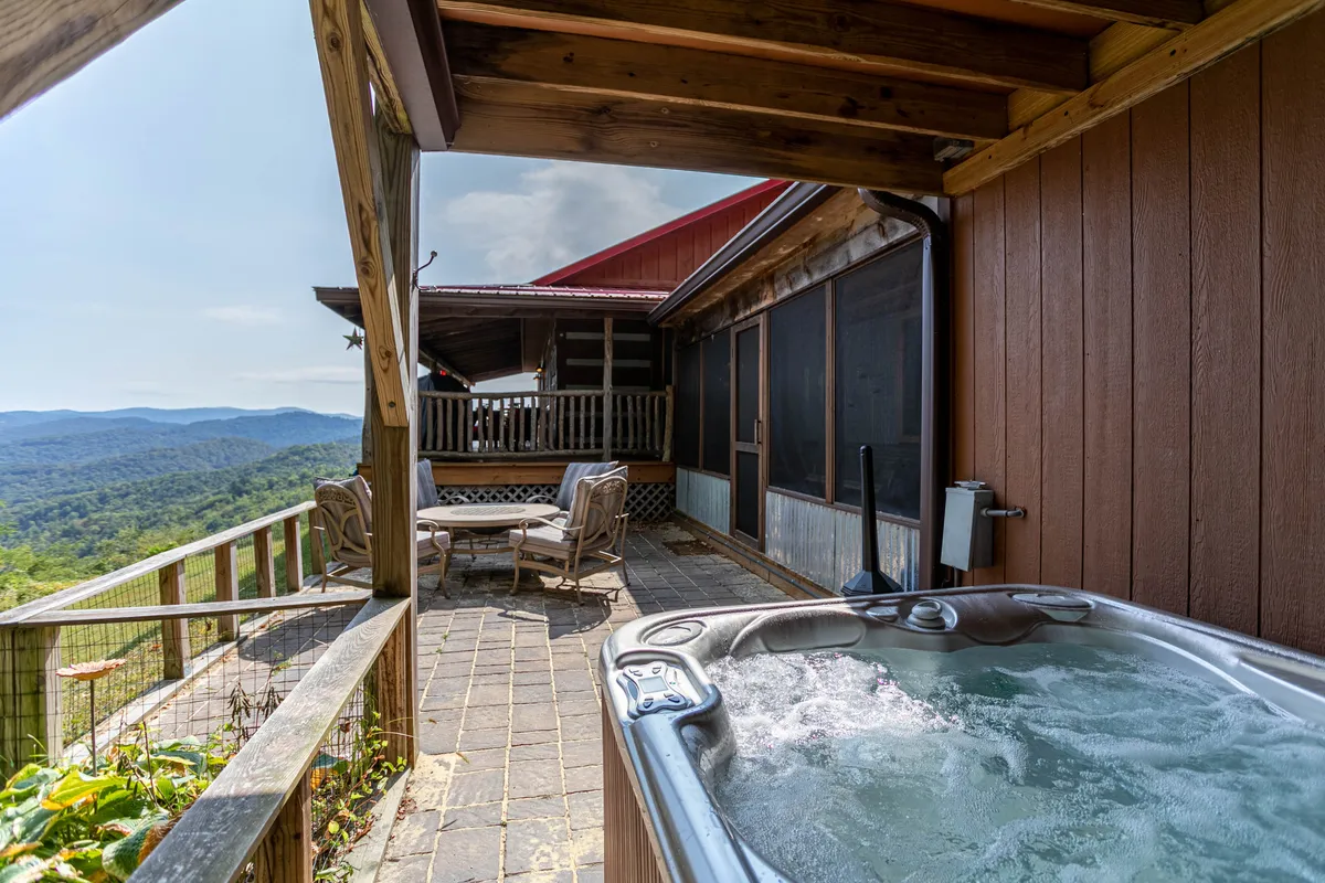 This image features a hot tub on a wooden deck overlooking long-range mountain views, accompanied by an outdoor seating area. The setting is serene, with a tranquil mood ideal for relaxation and social gatherings, matching the description of stargazing and unwinding after a day of adventure.