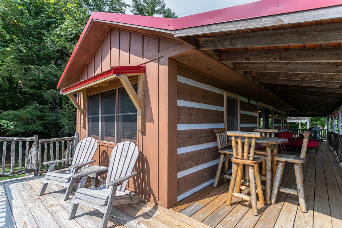 This image shows a log cabin exterior with a welcoming porch and wooden seating under a red roof, set against a backdrop of lush greenery. The scene suggests comfort and tranquility, inviting guests to relax and connect with nature right outside their door.
