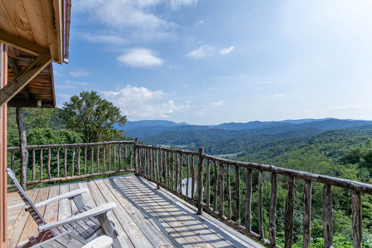 A serene view from the deck, framed by a wooden railing, overlooks rolling mountains and valleys. Comfortable deck chairs are positioned to maximize enjoyment of the tranquil setting, offering an ideal spot for wildlife watching, relaxation, or planning the next adventure.