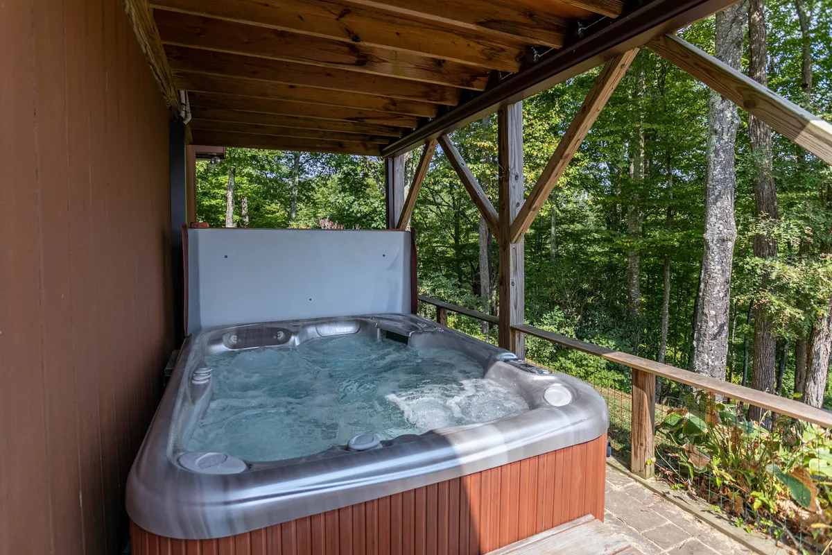 This exterior image features a tranquil hot tub nestled beside a wooden structure, surrounded by natural greenery. The setting evokes a sense of seclusion and relaxation, with the hot tub positioned to take in views of the landscape, ideal for evening stargazing or morning coffee outdoors.