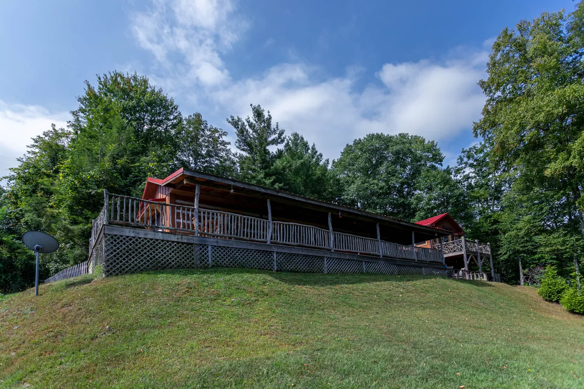 A tranquil exterior image showing a spacious wooden deck surrounded by lush trees, with the cabin’s red roof visible and the soft glow of natural light. The deck is an inviting space for relaxing on the porch, entertaining guests, or soaking in the beauty of the Blue Ridge landscape.