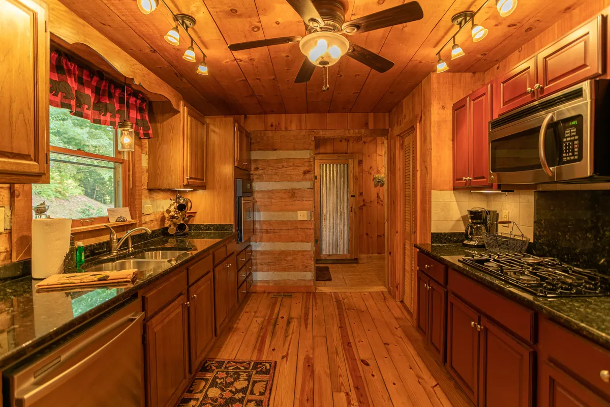 The kitchen is shown with rich wooden cabinets, sleek black granite countertops, modern stainless steel appliances, and a window with a view. The space is bright, functional, and designed for social cooking and entertaining.